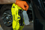 GrimmSpeed titanium front shim in place in a Subaru WRX STI yellow Brembo 6-piston front caliper - GrimmSpeed Thumbnail