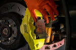 GrimmSpeed titanium rear shim in place in a Subaru WRX STI yellow Brembo 2-piston rear caliper - GrimmSpeed Thumbnail