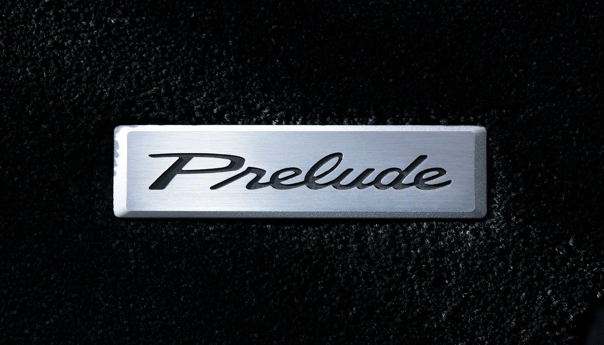 Close-up of the brushed metal Prelude logo plate on the Honda Access floor mat