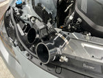 MST black silicone turbo inlet pipe beside the factory inlet in a grey BMW G-series B58 engine bay - MST Performance Thumbnail